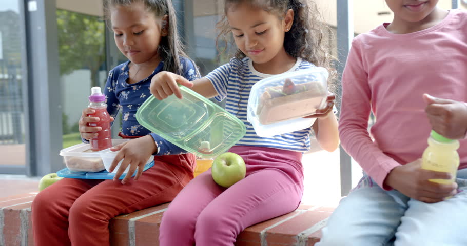 In school, three children sitting with lunchboxes and apple during break. Education, eating, childhood, unaltered, slow motion