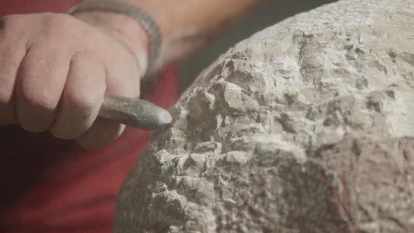 Close-up view about the moment of artistic stone carving with a man and his hammer tool, Italy.