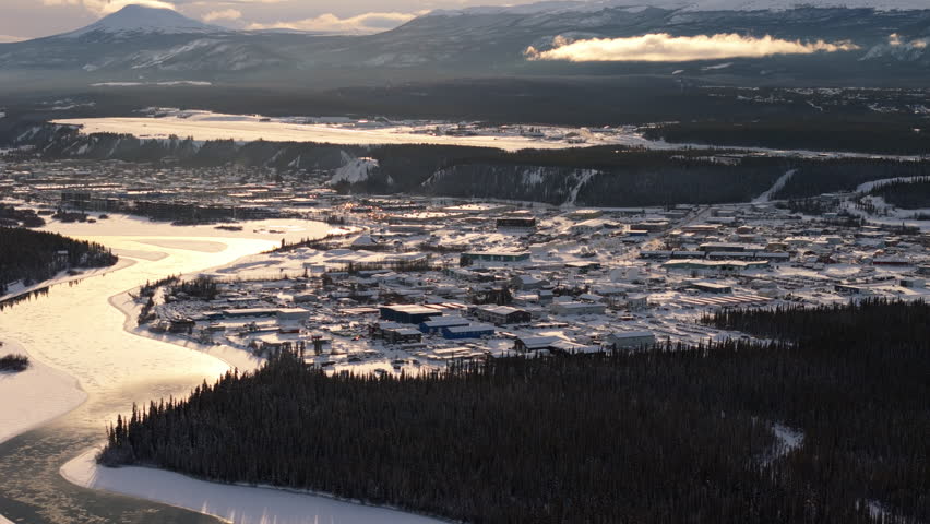 Gorgeous sunset aerial shot over Whitehorse, Yukon, with snow-covered landscapes and the glistening Yukon River reflecting the golden light.