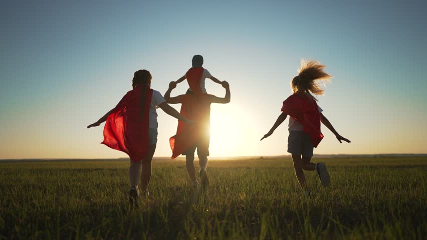 Happy family child play superheroes at sunset. child red capes run through open field embracing superhero fantasy. Family child bond during play at sunset. Superhero play strengthens family connection