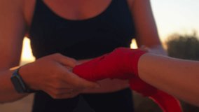 Sporty woman putting boxing wraps on the hand of female boxer at beach during sunset. Midsection close-up of the boxer and trainer preparing for practice in nature - Powered by Shutterstock - Get 15% off with code: PIKWIZARD15