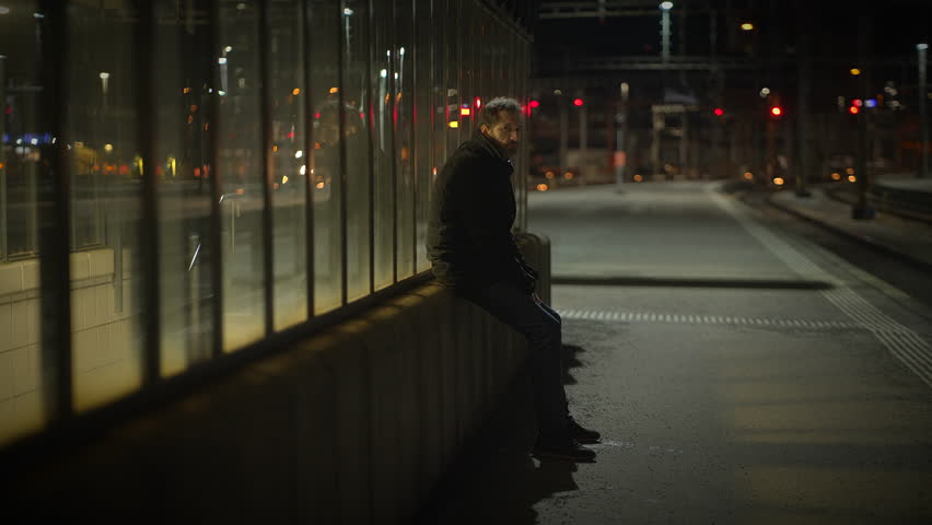 A Lonely sad man in Nighttime Reflection at the Urban Train Station Amidst the City Lights and Silence