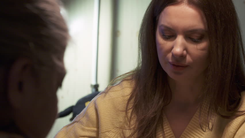 Woman dressed in yellow sweater sitting at table in living room. Relaxed woman holding teaspoon with cake and looking towards the left side as she converses with someone.
