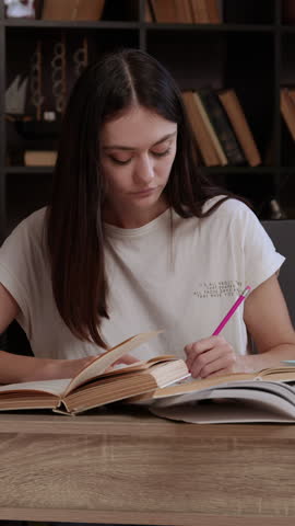 Tired young woman yawns with hand over mouth studying for exams in a modern library. Student holds hands to temples having headache from fatigue. Young lady studies at an office table. Student concept