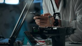 A person dressed in a lab coat is conducting electronics experimentation late in the evening. They are holding a smartphone while surrounded by various electronic components and tools on a table - Powered by Shutterstock - Get 15% off with code: PIKWIZARD15