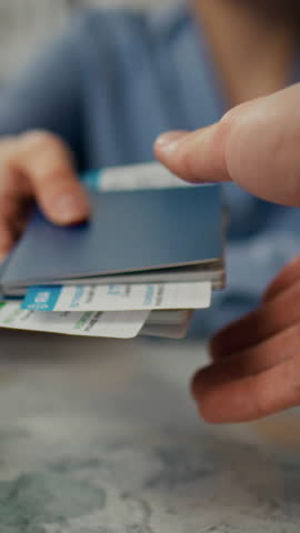 A person is extending a passport while holding travel documents at an airport. The background shows a bustling airport environment with travelers in motion, indicating a busy day of travel