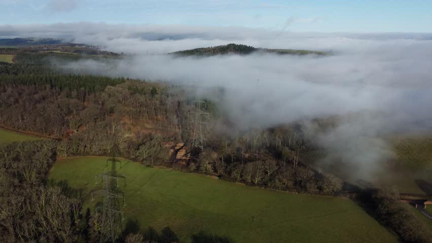 Aerial footage of National grid electricity pylons shrouded in mist across green Devon countryside. 