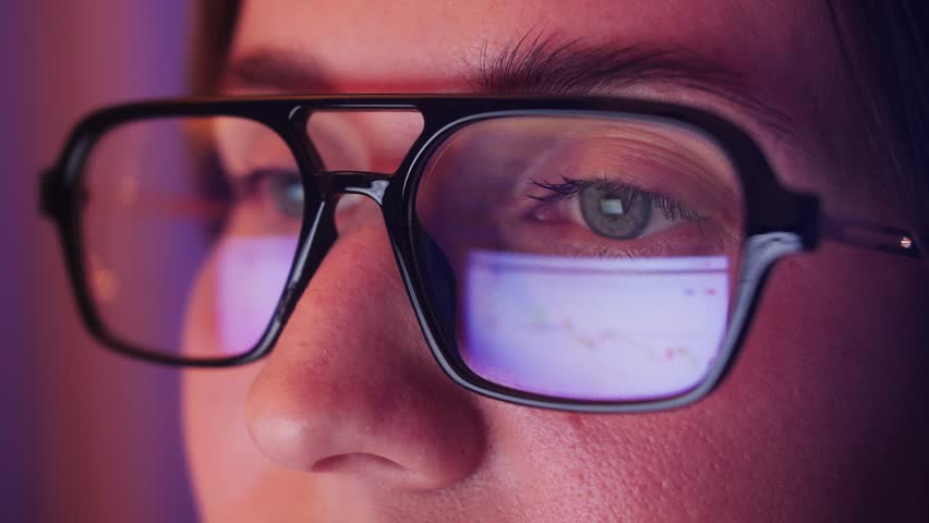 Close-up of eyes with glasses. Reflection of Web pages in the lenses of glasses. Business woman working on a computer in the dark. High quality 4k footage