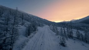 A tranquil snowy road winds through a forested mountain landscape as the sun sets, casting a warm glow over the serene winter scene. Nature captivates with its beauty. - Powered by Shutterstock - Get 15% off with code: PIKWIZARD15