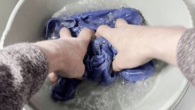 Closeup slow motion shot of a senior man’s hands squeezing a blue shirt in soapy water as he washes it in a plastic bowl. - Powered by Shutterstock - Get 15% off with code: PIKWIZARD15