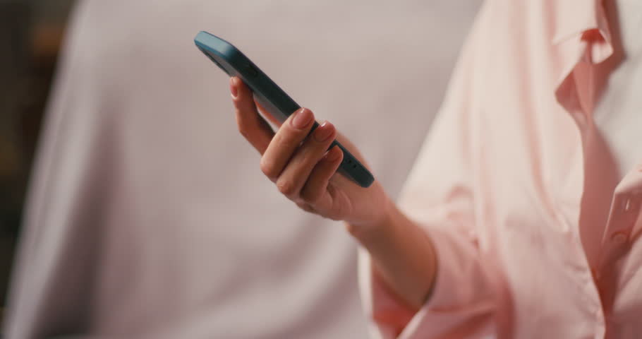 Woman hand holds smartphone scrolling social media. Female engages in online communication tapping phone screen sitting on sofa at home