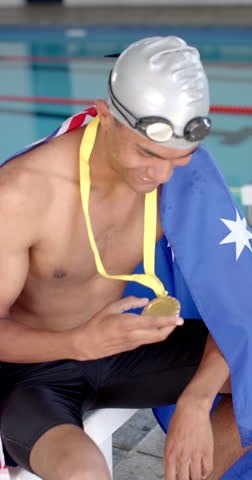 Vertical video: Strong and fit swimmer holding gold medal and smiling, wearing swim cap and goggles. Athlete, swimming, victory, competition, sports, award, slow motion