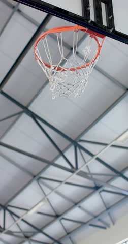 Vertical video: Scoring point, basketball going through hoop in indoor gym. Sports, gymnasium, athletic, competition, game, net