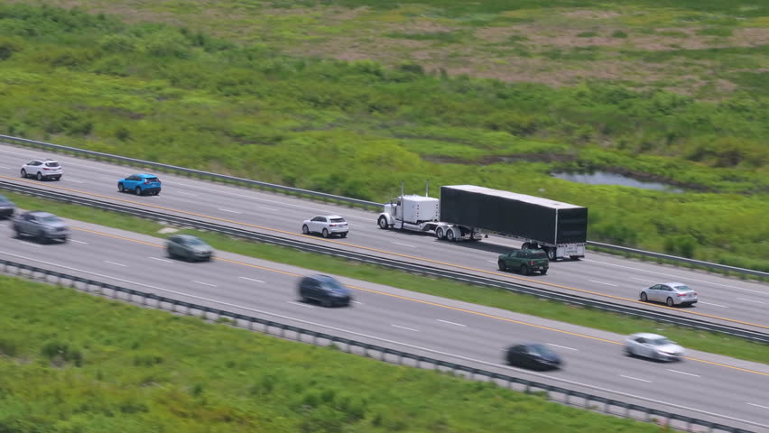 Aerial view of semi-truck driving on busy American interstate freeway. Delivering cargo concept.