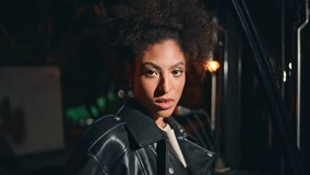 Trendy model posing at night area looking camera confidently closeup. Portrait gorgeous african american woman standing by forklift at dark street. Stylish curly-haired brunette enjoying nightlife. - Powered by Shutterstock - Get 15% off with code: PIKWIZARD15