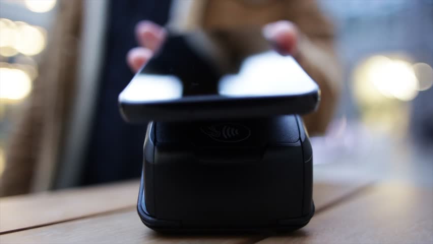 Contactless payment processing through smartphone beside pos terminal on wooden surface, demonstrating secure digital transaction using near field communication technology - Powered by Shutterstock - Get 15% off with code: PIKWIZARD15