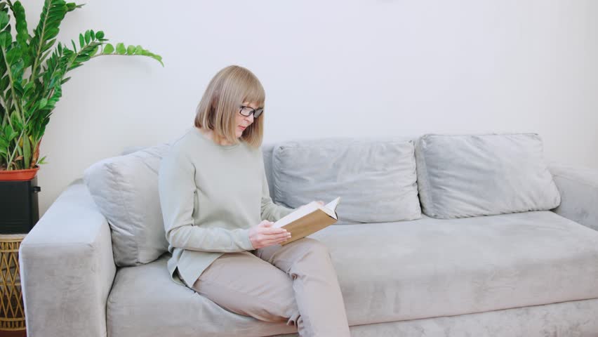 An elderly gray-haired woman in a soft sweater gets up from the sofa and sharply shows signs of discomfort, she has lower back pain, rheumatism