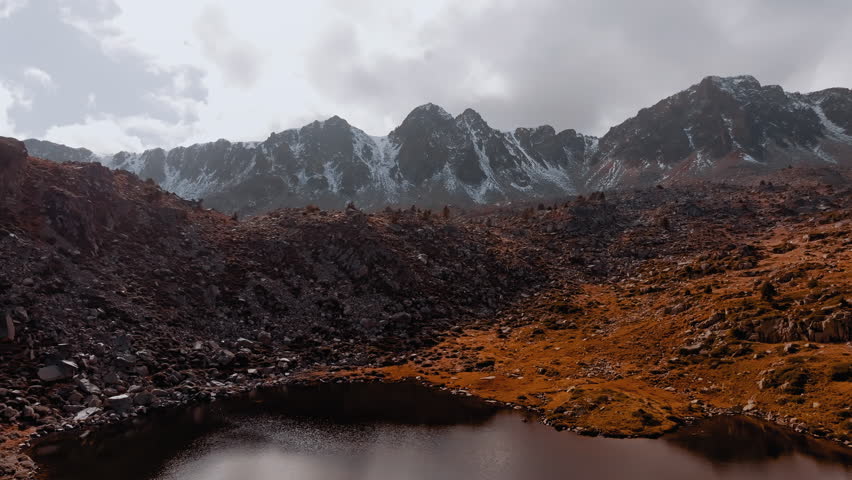 Mountains rise dramatically over a rocky terrain with patches of snow, showcasing the natural beauty of the Pyrenees in Spain. Autumn colors accentuate the landscape.
