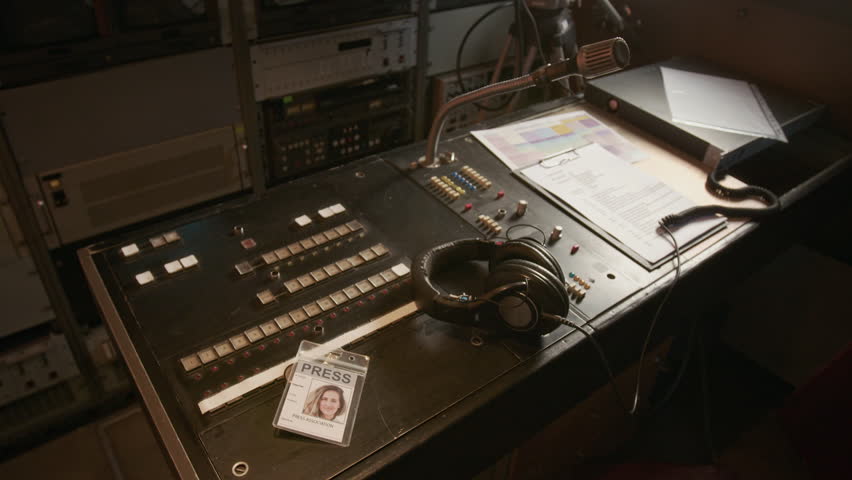 No people zoom-in shot of headphones and press pass or journalist ID card lying on production control desk, next to audio mixing console, show script, at workplace of broadcasting editor in TV van