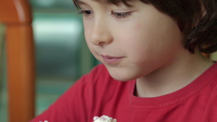 Child Eating Muffins Cupcakes Decorated With Sugar Cream. Boy Enjoying Vanilla Cupcakes with Frosting and Sprinkles. Unhealthy Junk Food. Hungry Sweet Tooth Child Bites Muffin with Sugar Frosting.