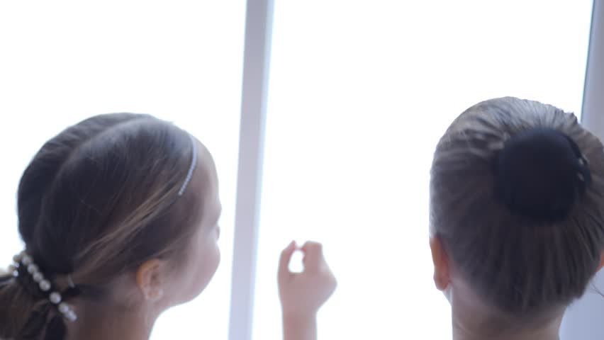 Two children looking out a window. One is wearing a headband