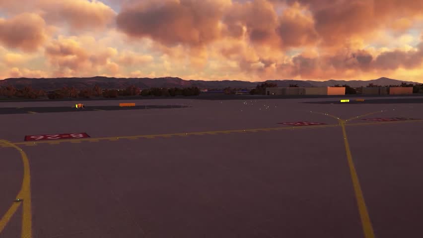 FPV or first person view aerial drone footage of a plane landing on an asphalt airstrip during sunset or sunrise. The landing strip has white and yellow road marking and orange clouds are in the back.