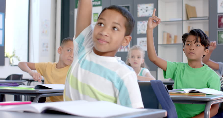 Biracial boys and girls raise their hands in a classroom at school. Eager students participate in a lesson, showcasing a learning environment, slow motion.