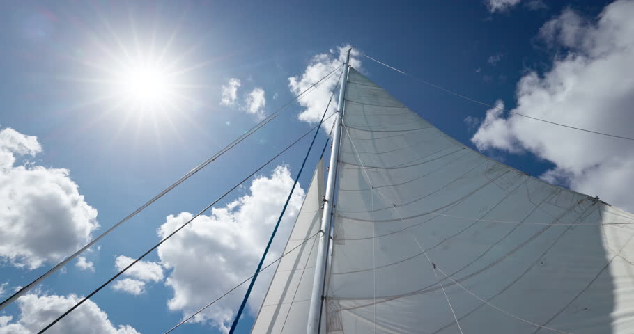 Sun shining through mast of sailboat with blue sky and white clouds