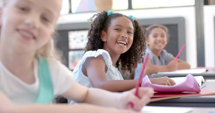 Biracial and Caucasian girls enjoy a school classroom activity. They're engaged in a fun learning experience with pencils and notebooks, slow motion.