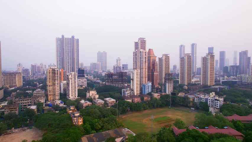 A morning aerial moving drone shot of the high-rise buildings or skyscrapers in the developing urban cityscape of Mumbai city surrounded by the green tree cover. Infrastructure, real estate concept