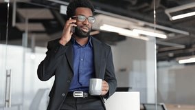 Stylish businessman talking on phone and drinking coffee in modern office. Young African American male entrepreneur enjoying a workday break. - Powered by Shutterstock - Get 15% off with code: PIKWIZARD15