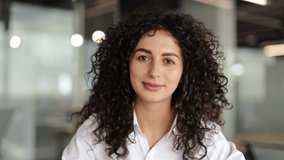 Confident businesswoman with curly hair sits in a modern office, actively communicates during a video call, looking directly at the camera. - Powered by Shutterstock - Get 15% off with code: PIKWIZARD15