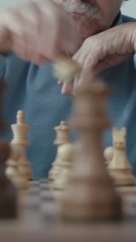 Vertical Screen: Senior man playing chess, he is moving a piece on the chessboard