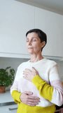 Peaceful mature woman engages in deep breathing exercises with hands placed on chest at home. Relaxed female mindfulness, serenity and stress free meditation, slow time with yourself in solitude - Powered by Shutterstock - Get 15% off with code: PIKWIZARD15