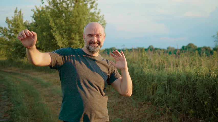 Bald male dancing joyfully with beaming smile, waving hands expressively. Guy moving in carefree rhythm, using hand gestures to convey excitement. Male performing upbeat dance, radiating happiness