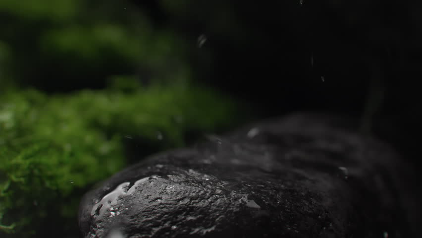 Water droplets falling on a rock surface close up. Aqua drops falls and splashing on a stone. Concept of natural springs and wellness or beauty products. Cold mineral water in super slow motion
