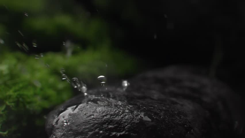 Water droplets falling on a rock surface close up. Aqua drops falls and splashing on a stone. Concept of natural springs and wellness or beauty products. Cold mineral water in super slow motion