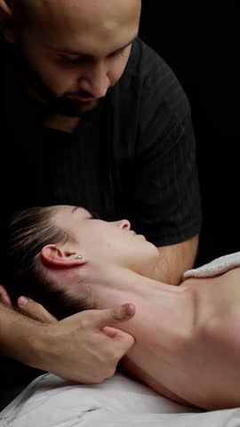 Professional physiotherapist massaging woman's neck, targeting muscle tension with specialized manual therapy techniques in dim studio setting