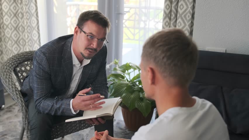 A smiling psychotherapist leans toward the patient, evaluating their emotional state. He explains methods to overcome stress and anxiety, offering support and confidence in the treatment process.