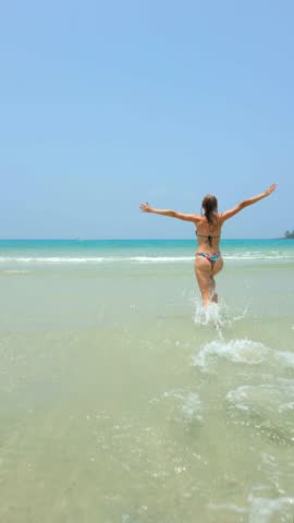 Happy Caucasian woman runs and jumps into the turquoise sea on paradise beach. Concepts of freedom, tropical vacation, and travel