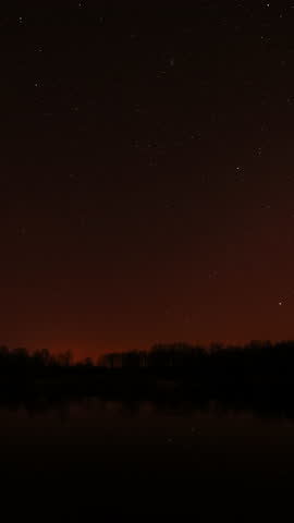Real Colorful Night Stars Above Lake River. Natural Starry Sky Background Backdrop. Time Lapse. Vertical Shot. Glowing Stars Reflected In Lake River Water. Natural Starry Sky Background Backdrop