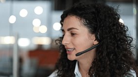 Friendly businesswoman with curly hair talks on headset in modern office. Woman enjoys pleasant conversation at workplace. Corporate communication and client service concept. - Powered by Shutterstock - Get 15% off with code: PIKWIZARD15