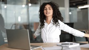 Beautiful businesswoman with curly hair stretching her arms and back at the office desk. She takes a deep breath and smiles. - Powered by Shutterstock - Get 15% off with code: PIKWIZARD15