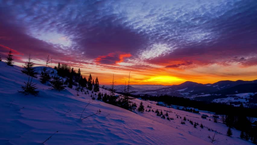 A scenic winter morning with the sun rising over snow-covered peaks, casting long shadows and a warm glow over the frozen landscape.