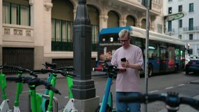 Young man scanning QR code with smartphone app to unlock electric scooter sharing service on city street. Modern transportation, eco-friendly travel, and technology integration for urban mobility - Powered by Shutterstock - Get 15% off with code: PIKWIZARD15
