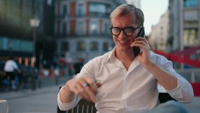 Confident Caucasian businessman making phone call while working at café. Wearing glasses and holding pen, successful freelancer discusses business strategies during productive outdoor work session - Powered by Shutterstock - Get 15% off with code: PIKWIZARD15
