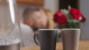 Wooden table featuring red roses, ceramic mugs, blurred romantic couple embracing near water jug, creating intimate valentine's day morning scene.Celebrating valentine's day or anniversary - Powered by Shutterstock - Get 15% off with code: PIKWIZARD15