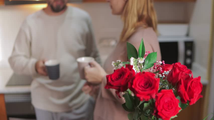 Intimate couple enjoying morning coffee, red roses highlighting cozy kitchen, sharing gentle connection and warm relationship.Celebrating valentine