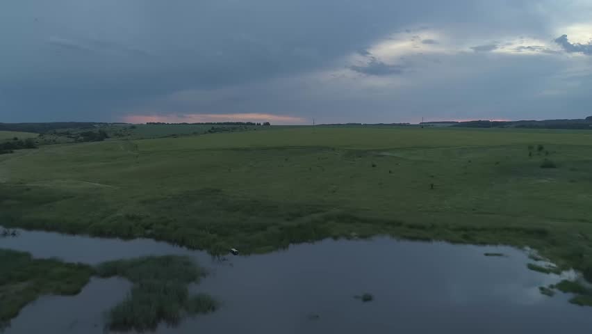 Cloudy sky with a field of grass and a body of water. The sky is dark and the water is calm. Evening summer natural landscapes of the Nizhny Novgorod region Russia