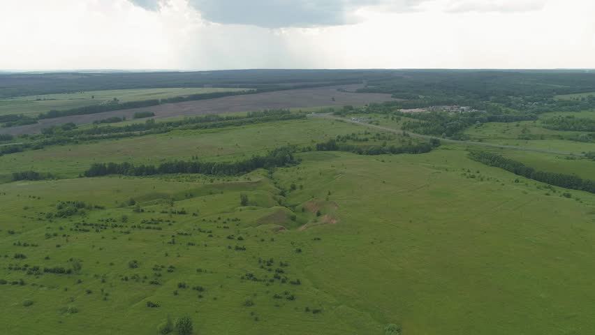 Large, open field with a few trees scattered throughout. The sky is cloudy and the sun is not visible. Evening summer natural landscapes of the Nizhny Novgorod region Russia